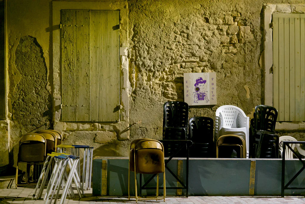 Plastic and metal chairs stacked against an ochre wall, a small poster pinned above them