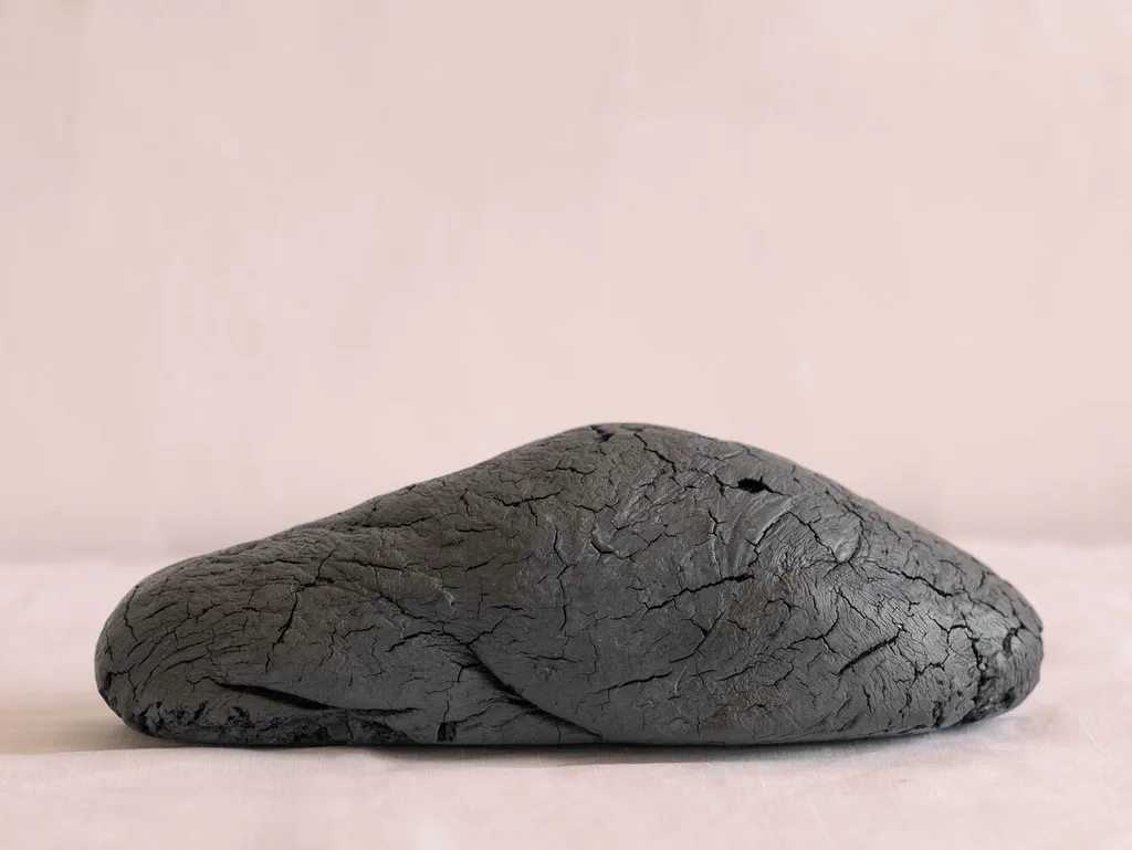 Lump of dark cracked raw liquorice on a plain ground