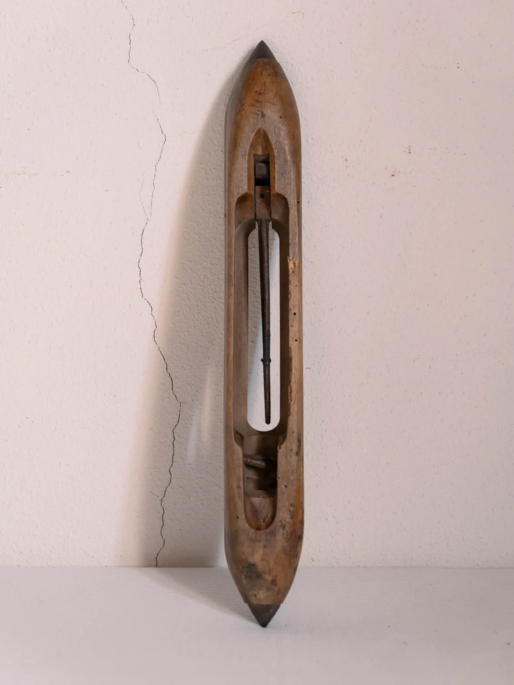 Weaver’s wooden shuttle standing against a cracked wall