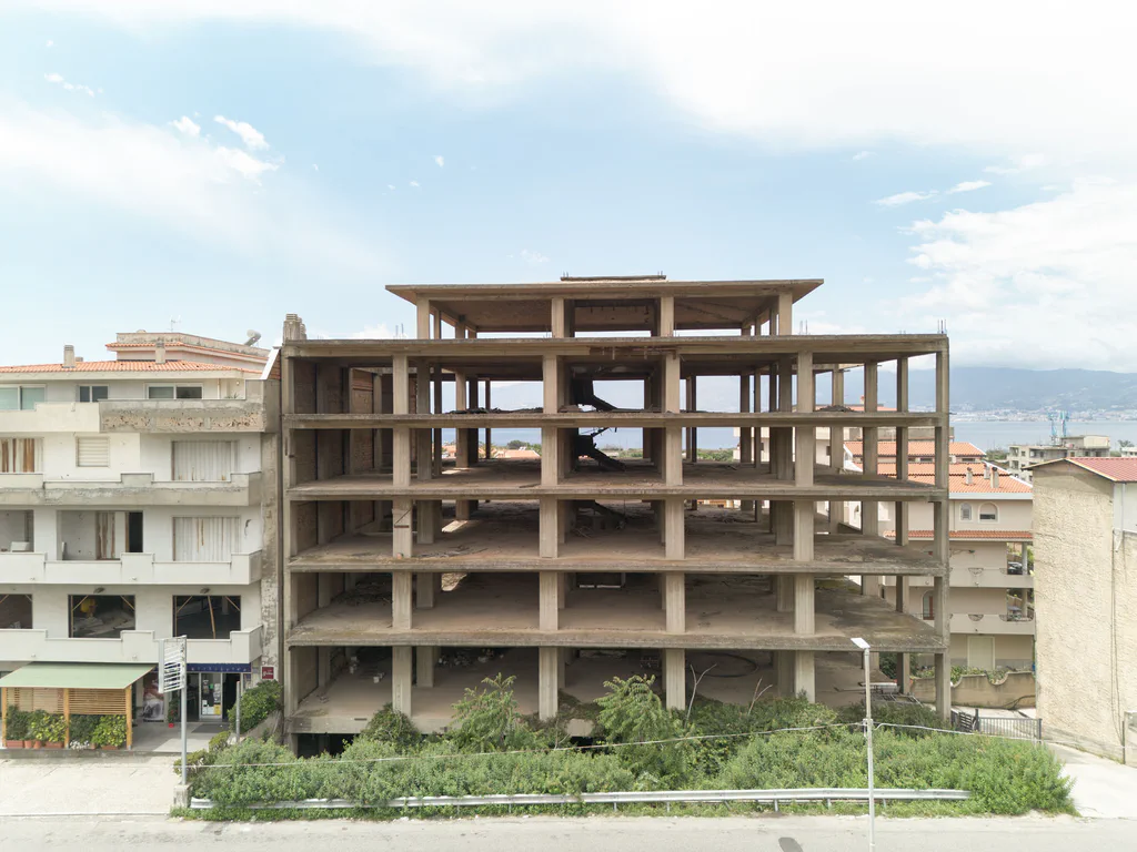 Unfinished reinforced concrete frame of a multi-storey building standing between inhabited blocks