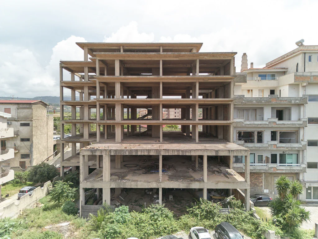 Abandoned four-storey building shell, beams and pillars exposed, vegetation growing at its base