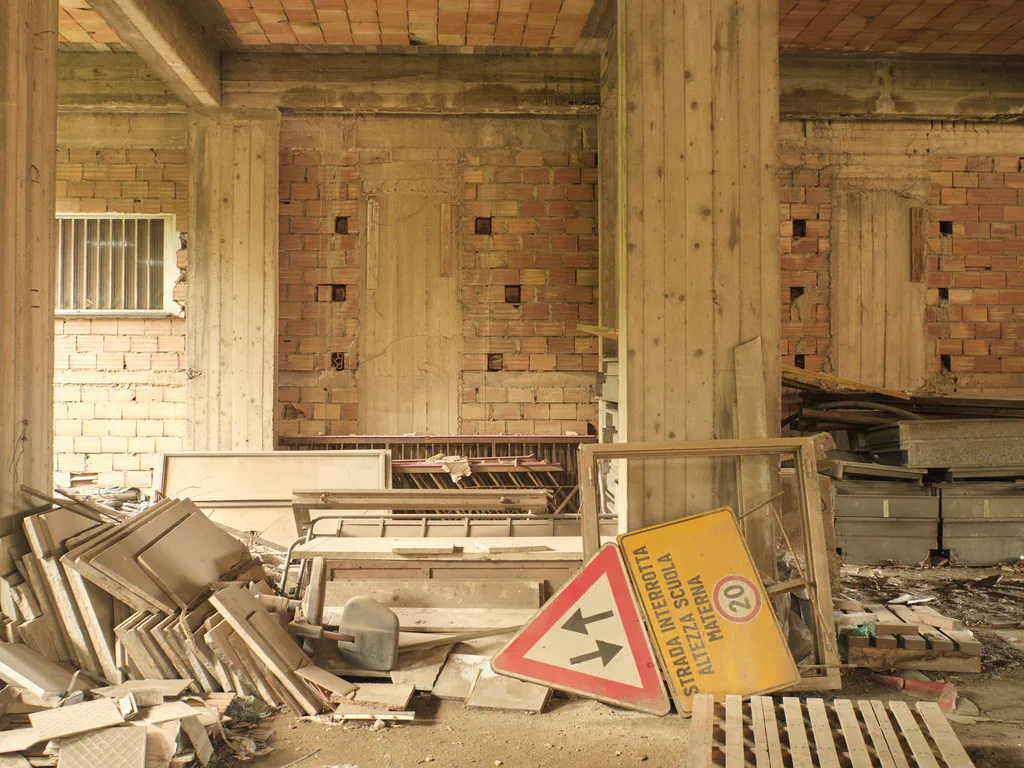 Bare interior with brick walls and concrete pillars, stacked timber and a no-entry sign