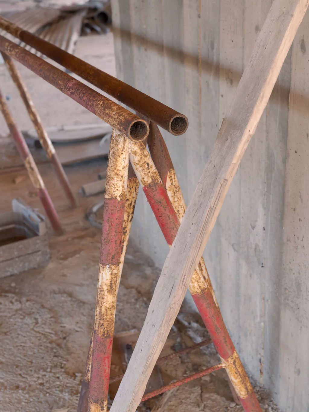 Rusted metal tubes and bars leaning against a concrete pillar