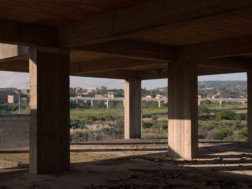 Open ground floor of an unfinished building, the town visible between the pillars