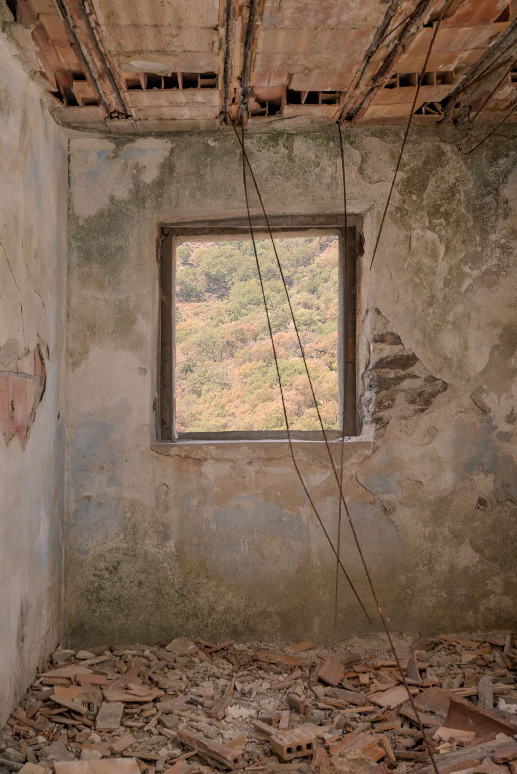 Empty room with a broken roof, a window opening onto the green hillside, floor covered in fallen tiles