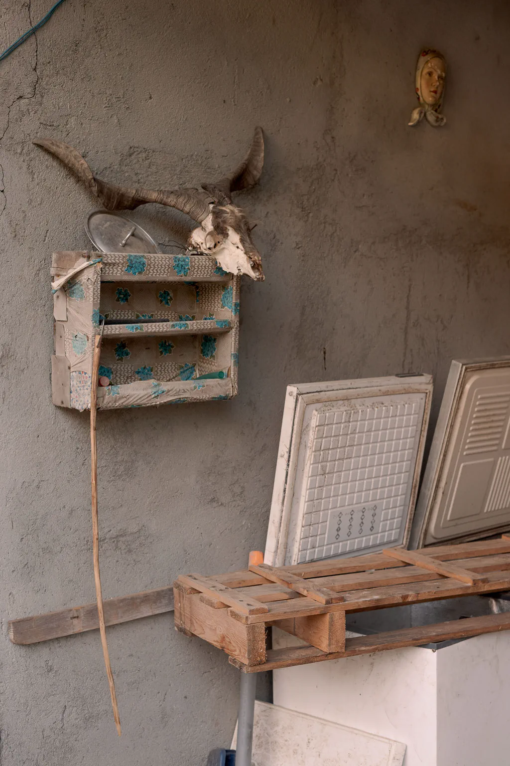 Corner of a workshop: animal horns and a skull above a wooden shelf, picture frames stacked below