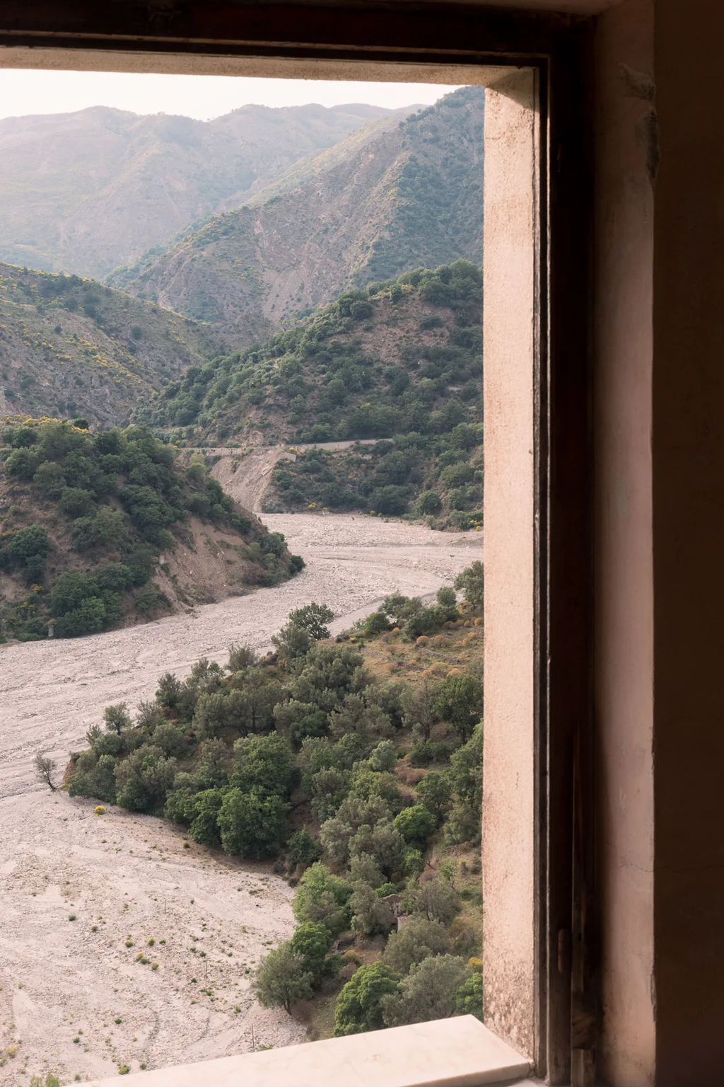 View from a doorway onto a wide dry riverbed running between wooded mountains
