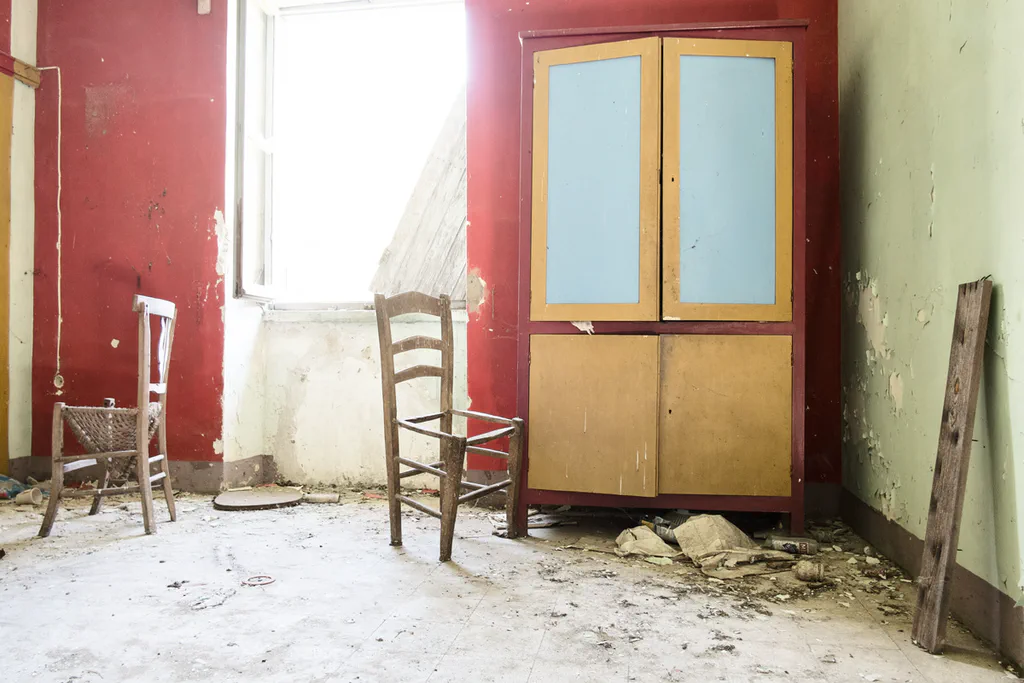 Room with red walls, two chairs and a yellow wardrobe, plaster falling from the ceiling
