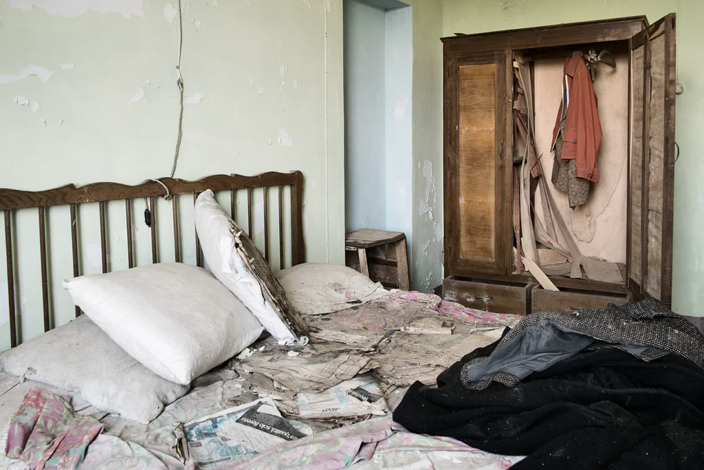 Abandoned bedroom, a bed piled with cushions and clothes, a wardrobe standing open
