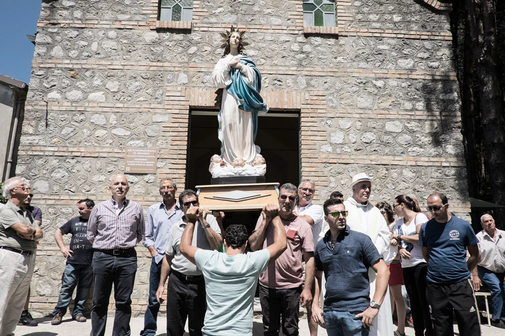 Men carrying a statue of the Virgin on their shoulders outside a stone church