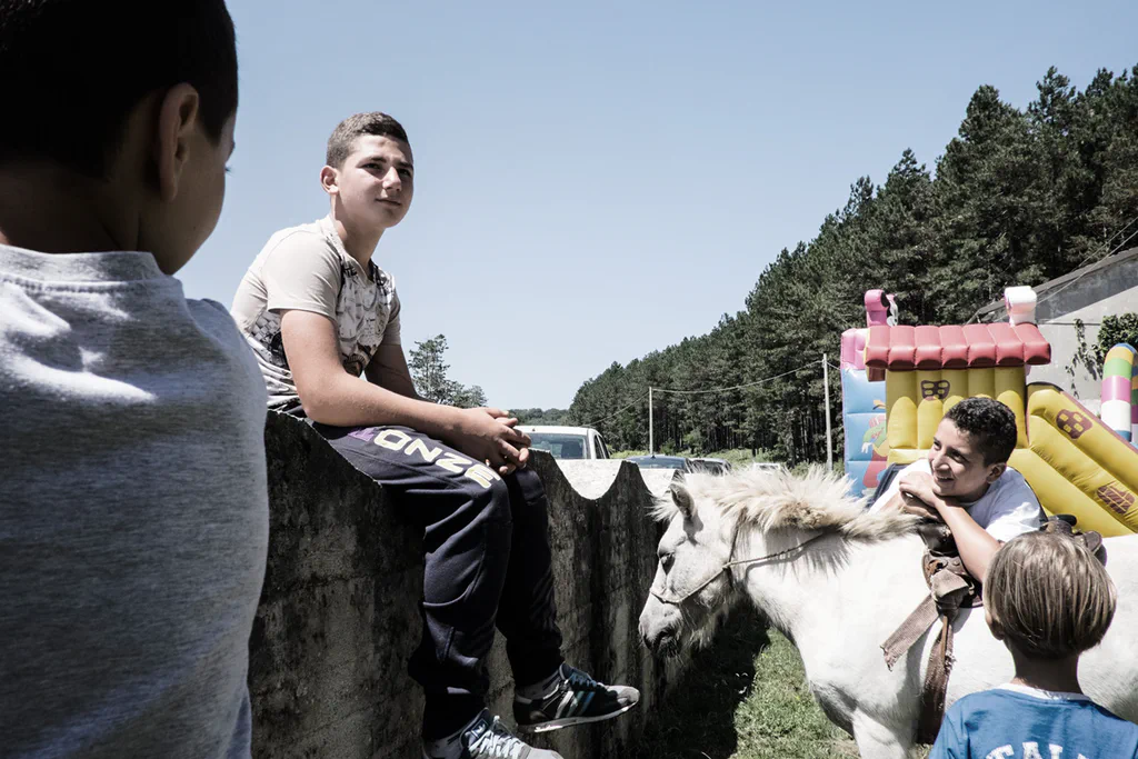 Children beside a white horse at a village fair, an inflatable castle behind