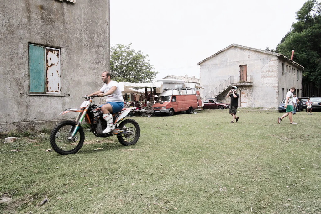 Man riding a motocross bike across the grass in front of a house