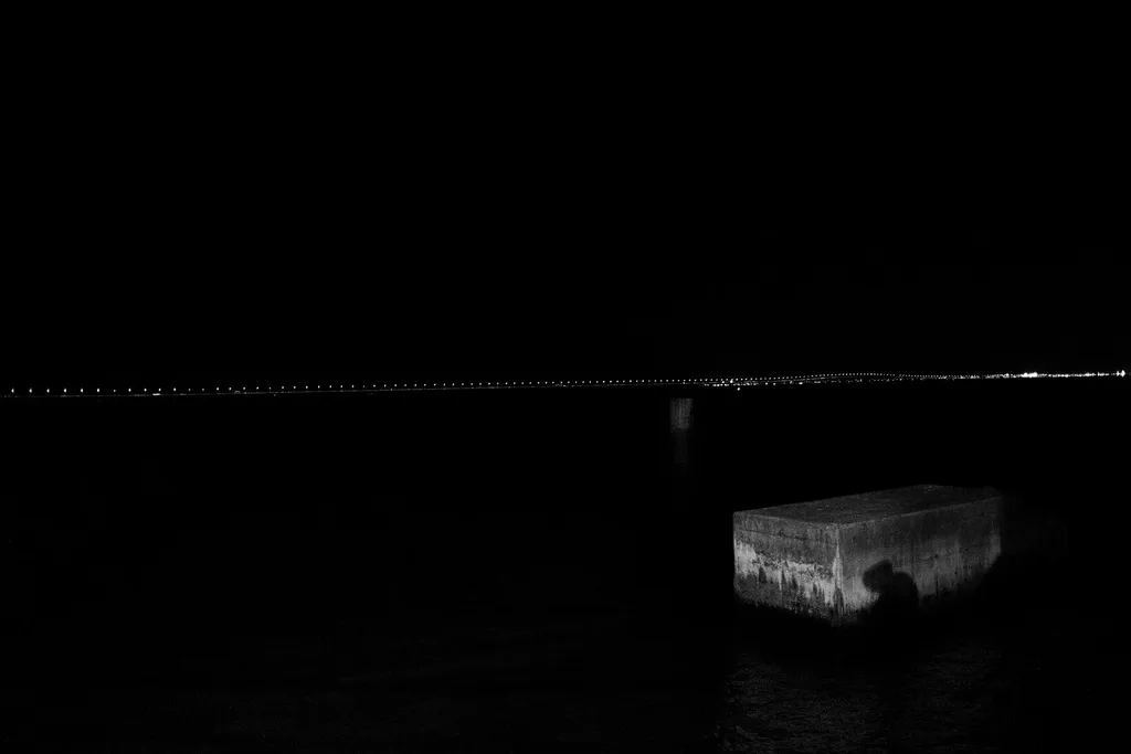 Concrete block in the water at night, the lit bridge on the horizon