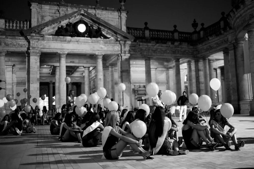 Contestants waiting on the steps of a neoclassical building, balloons among them