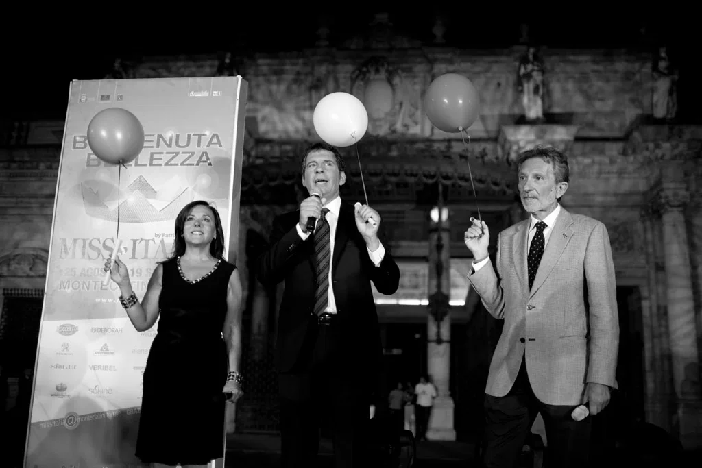 Presenters on an outdoor stage holding balloons in front of the event banner