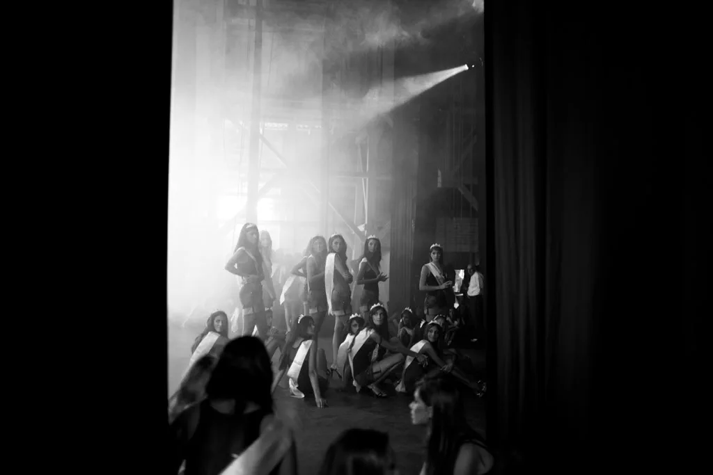 Contestants sitting in a dark hall, a shaft of light falling across them