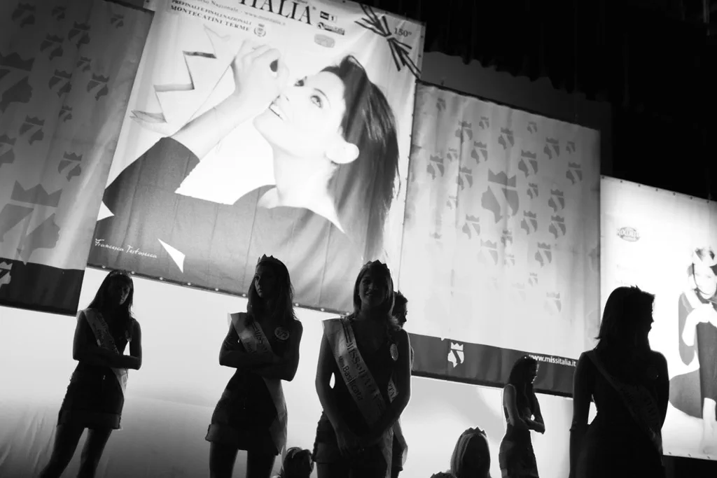 Contestants silhouetted against a lit advertising panel backstage