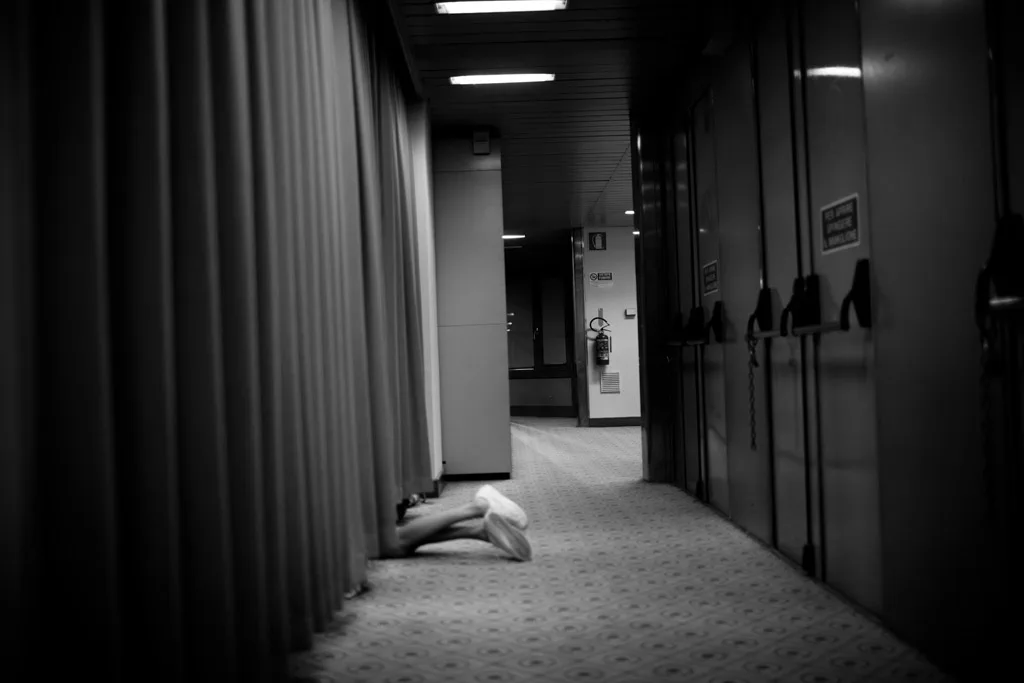Empty corridor backstage, a figure crouching at the far end