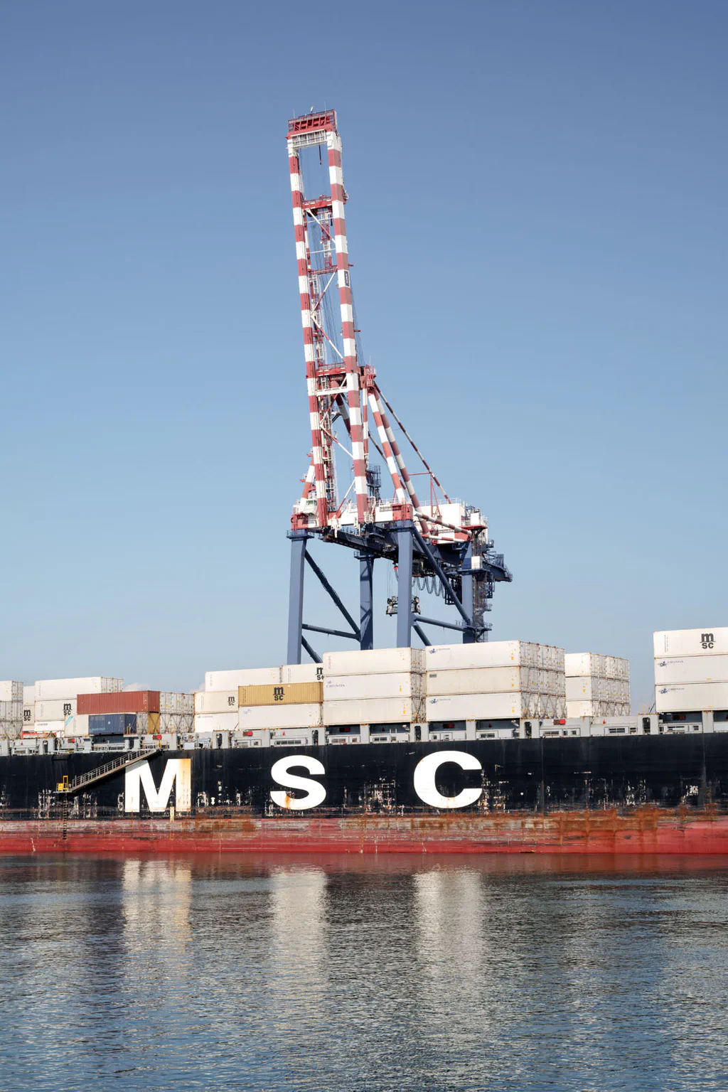 Red and white crane against a clear sky above a moored ship