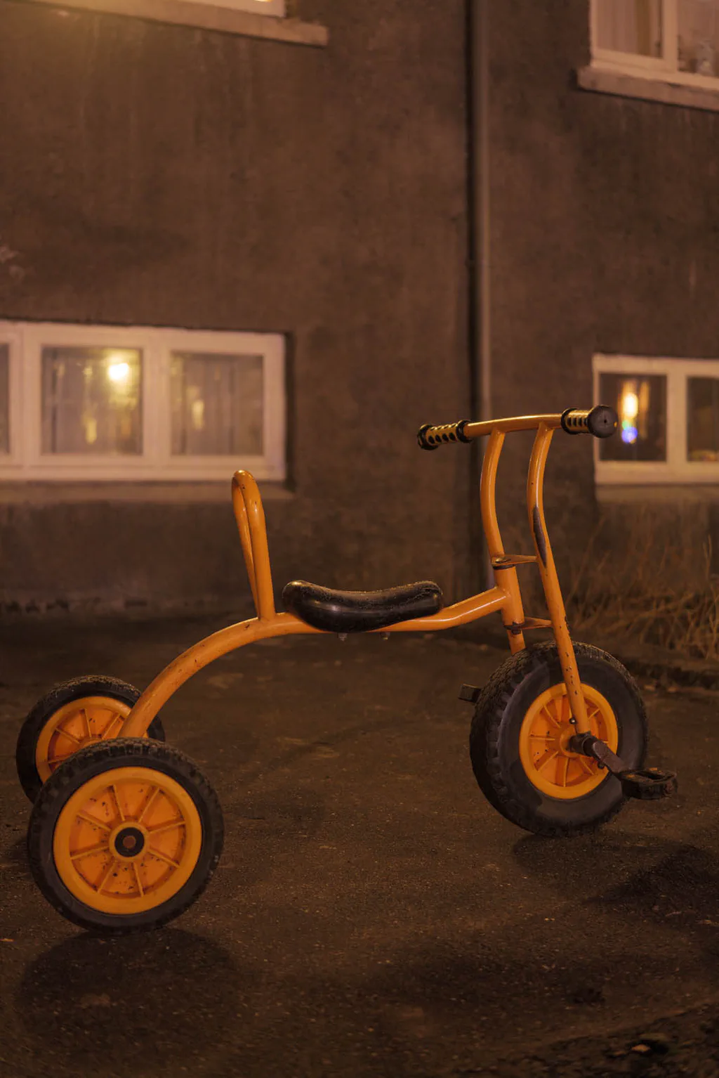 Child’s yellow tricycle standing alone outside a house at night