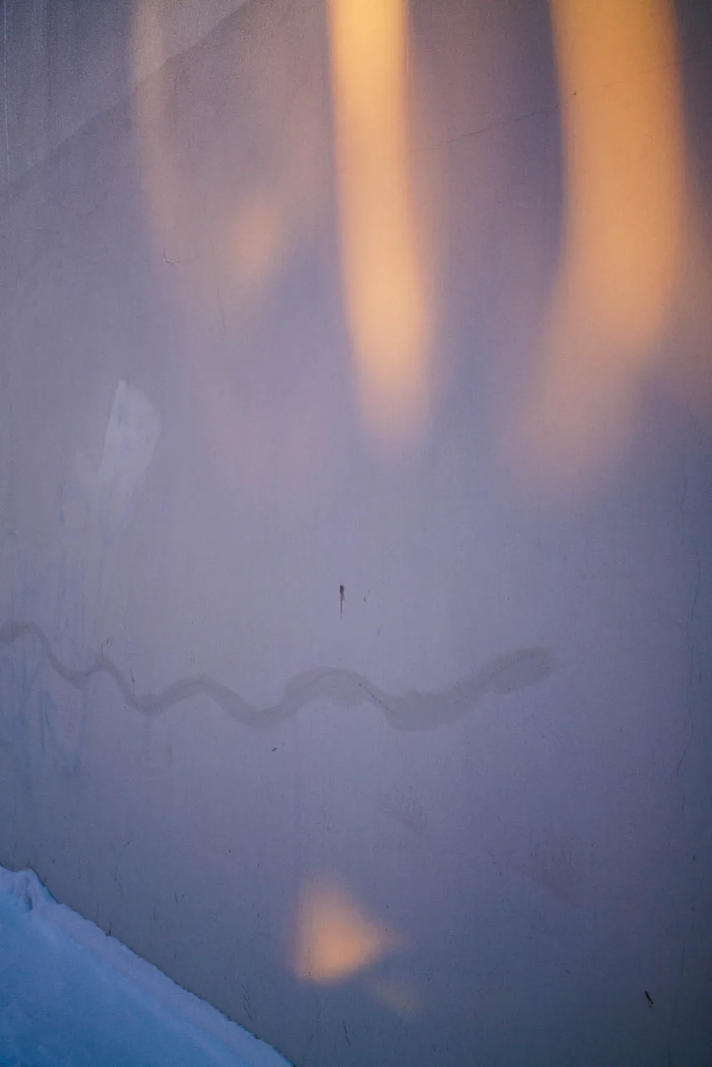 Pale wall washed by shifting light, a wire casting a wavering shadow
