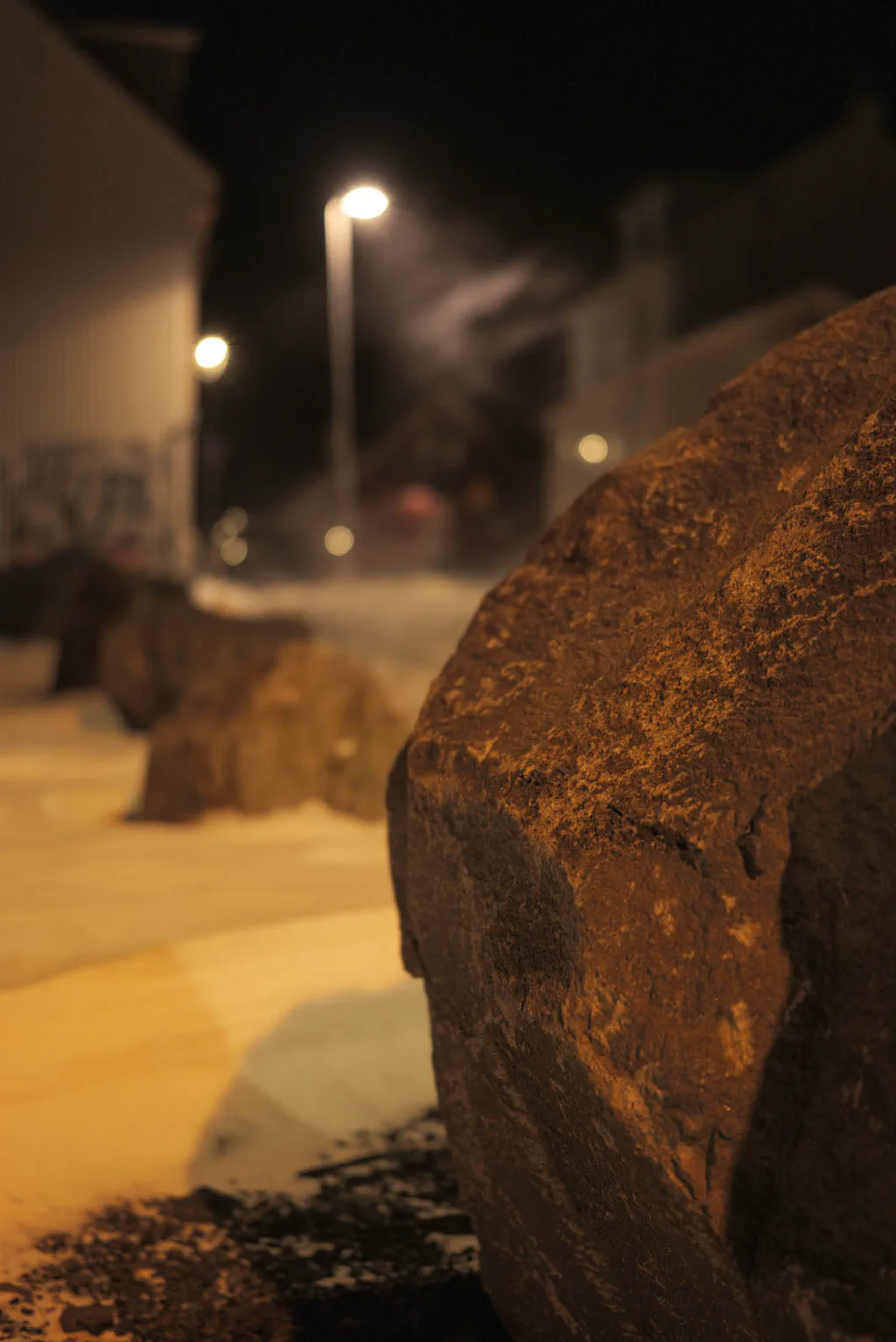Large boulder beside a road under streetlights, snow on the ground