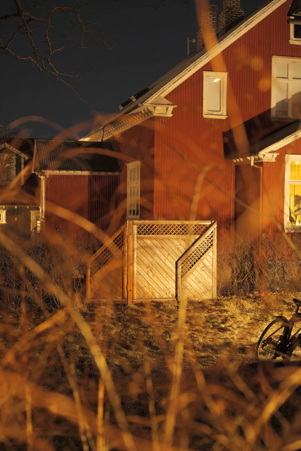 Red timber house glowing behind tall dry grass