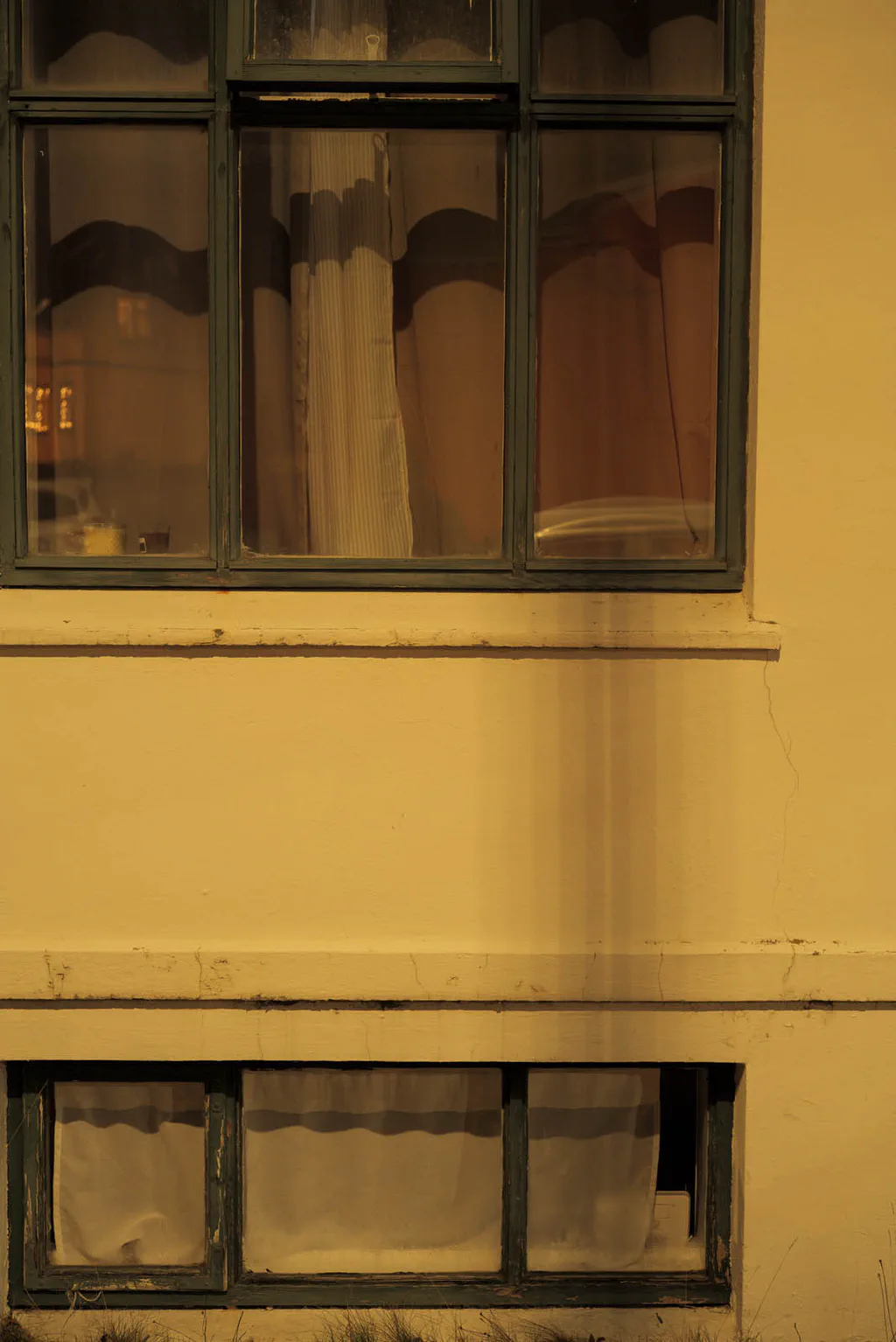 Windows of a yellow house at night, curtains drawn