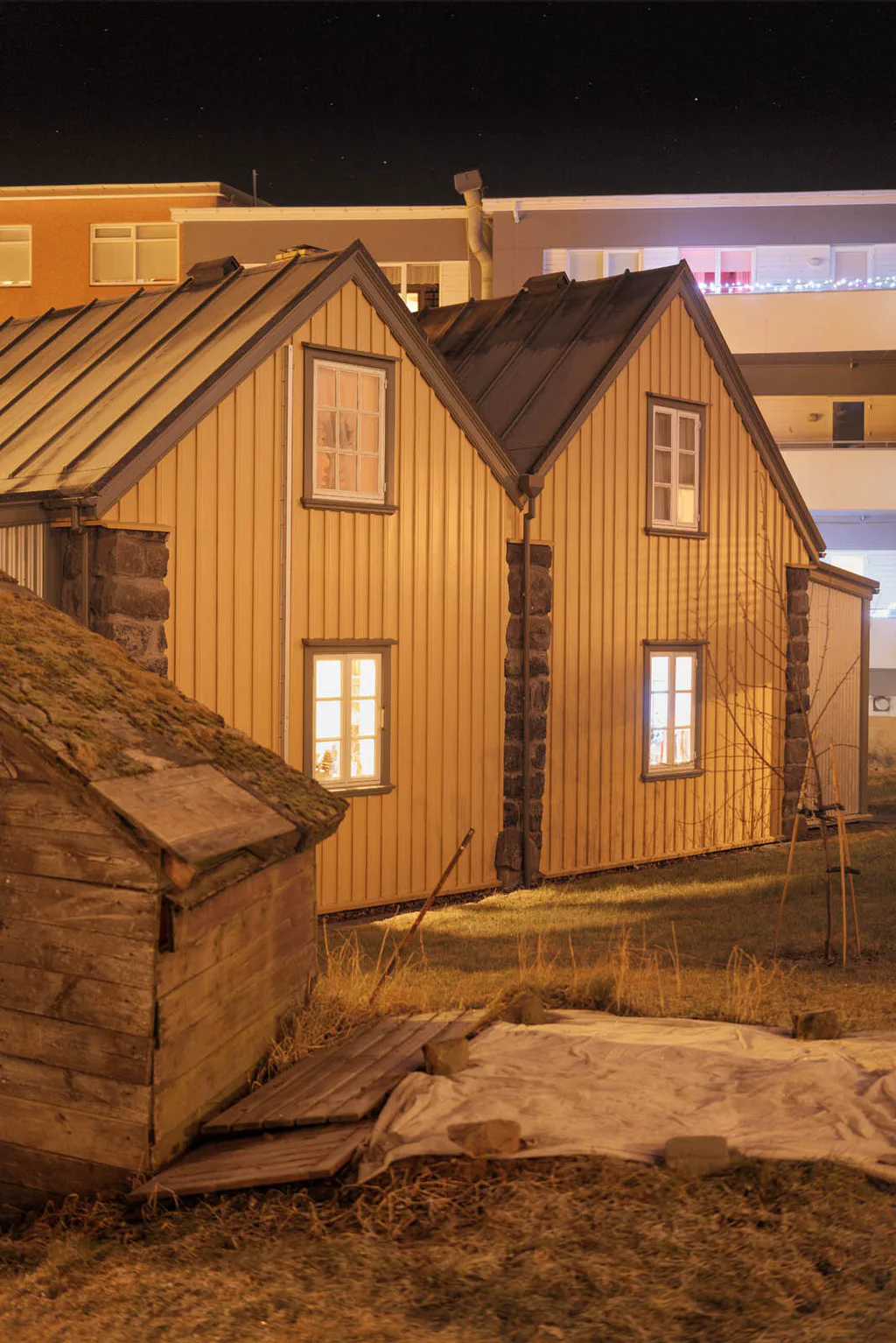 Timber houses with pitched roofs, lights on, seen at night