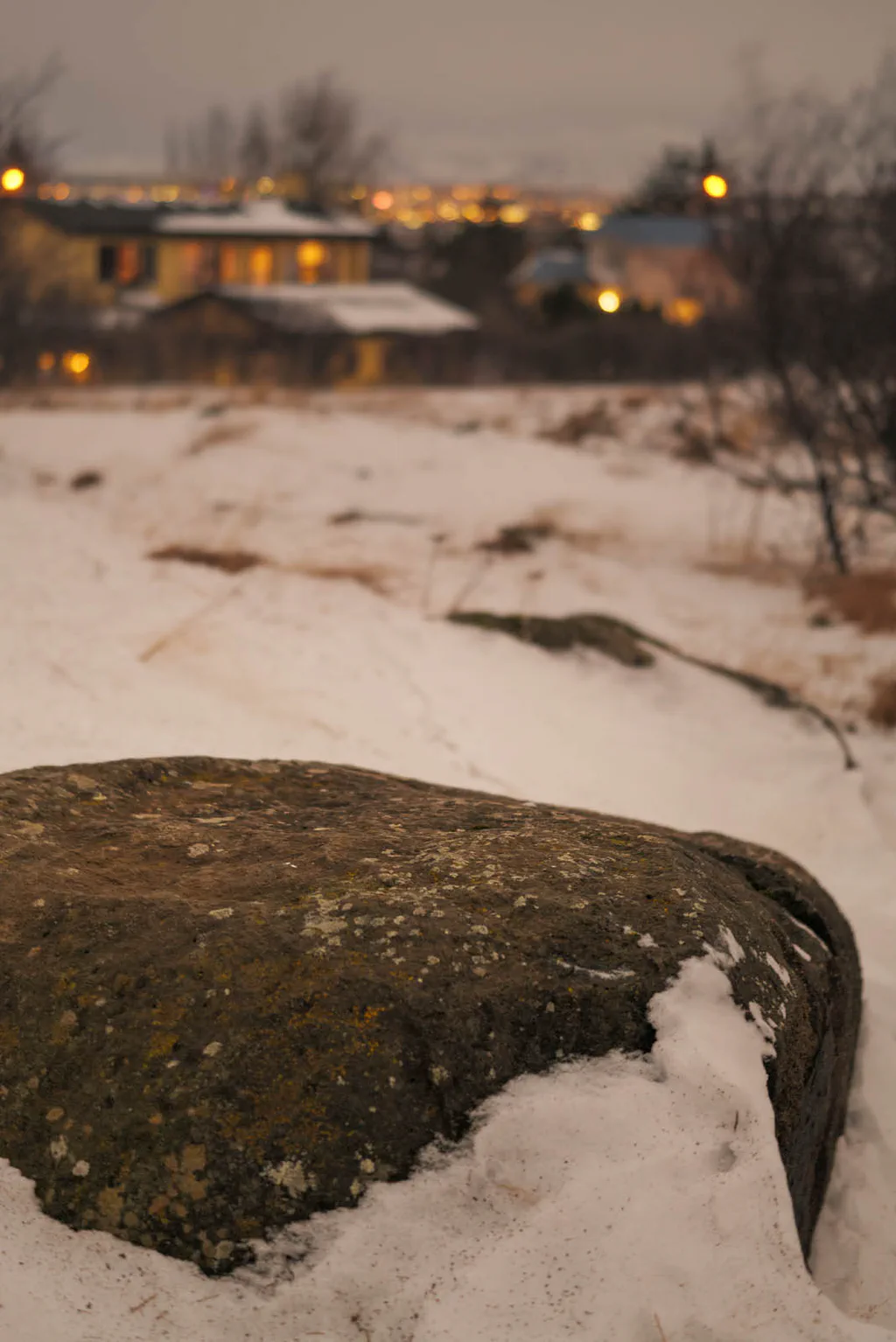 Snow-covered rock at the edge of town, the lights of the city beyond