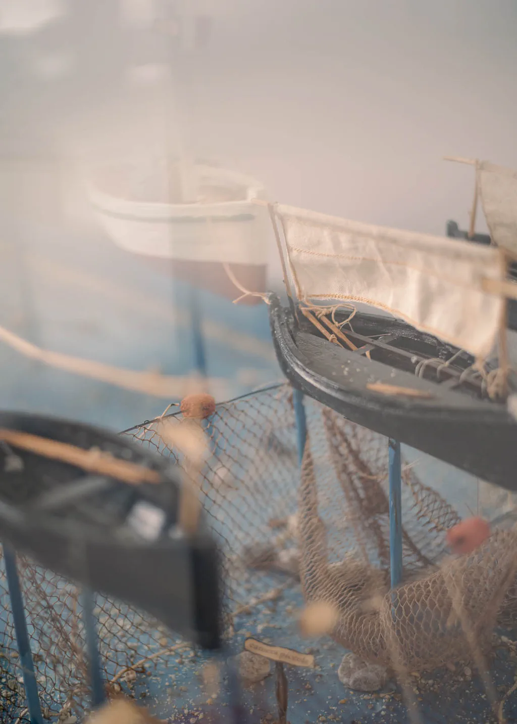 Model fishing boats and nets behind museum glass, reflections on the surface