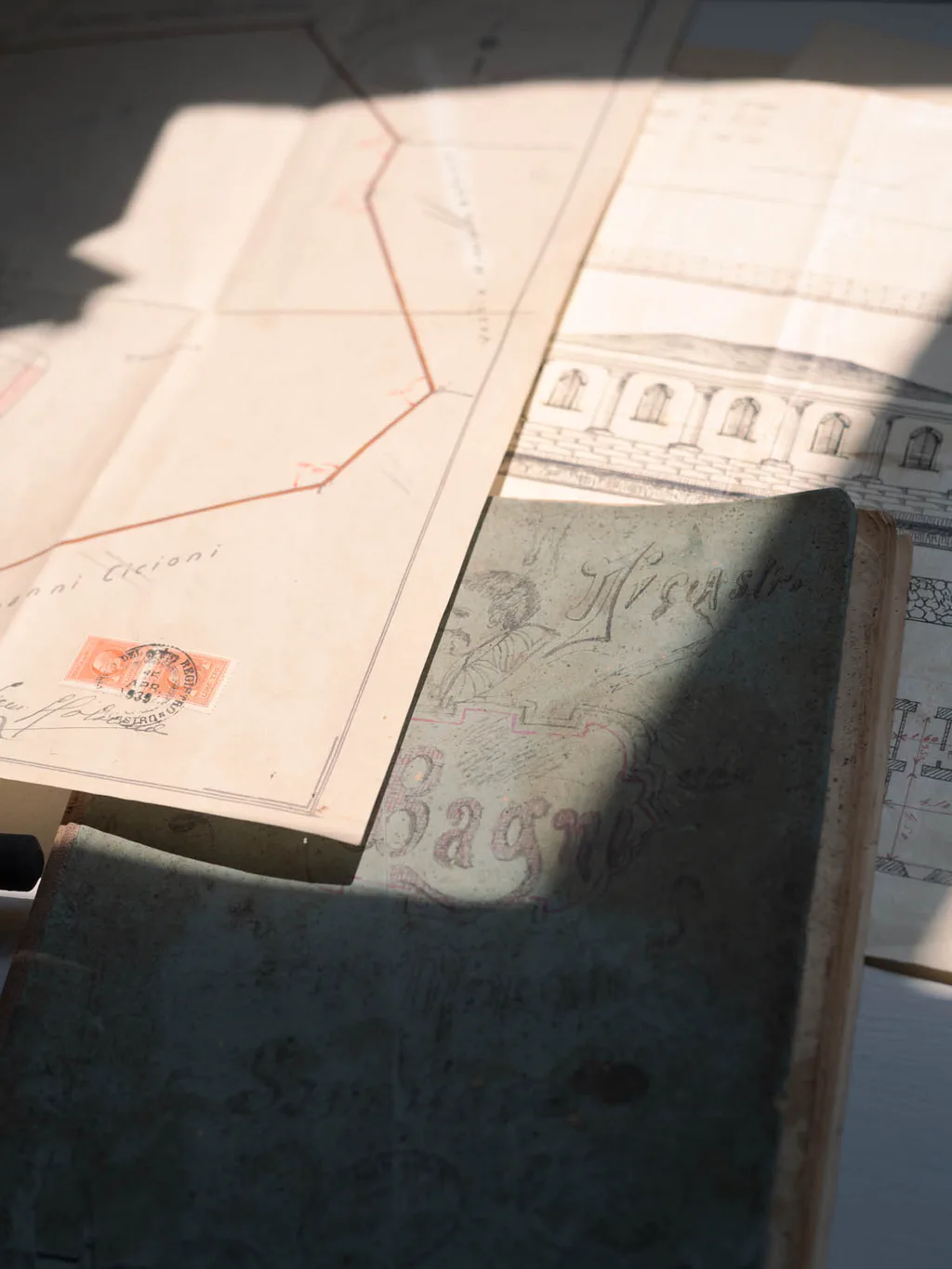 Open ledgers and hand-drawn plans in a display case, a revenue stamp on the top sheet