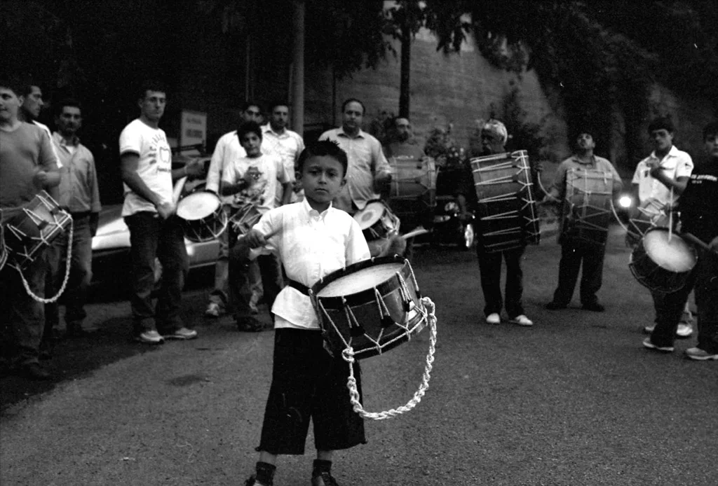 Boy holding a drum in a street procession, other drummers around him