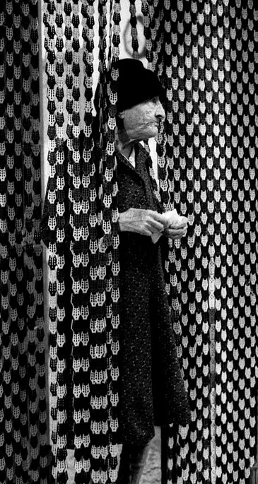 Elderly woman standing in a doorway behind a beaded fly curtain