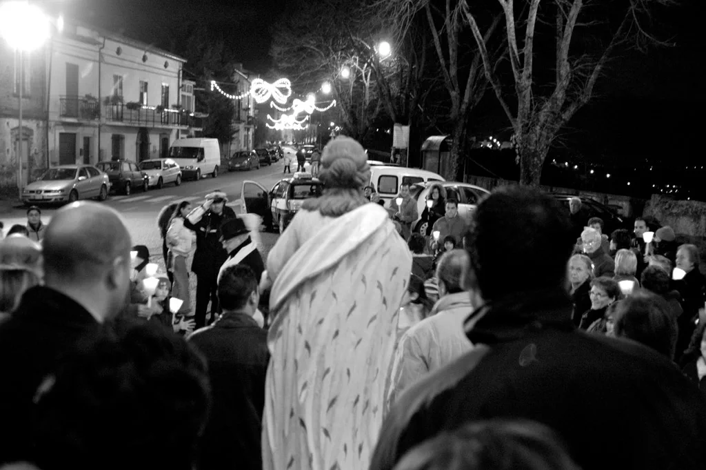 Procession moving along a street at night, candles and lights among the crowd
