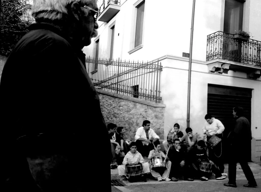 Onlookers seated along a street watching a procession pass
