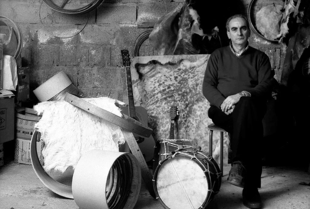 Drum maker seated in his workshop among frames, skins and finished drums