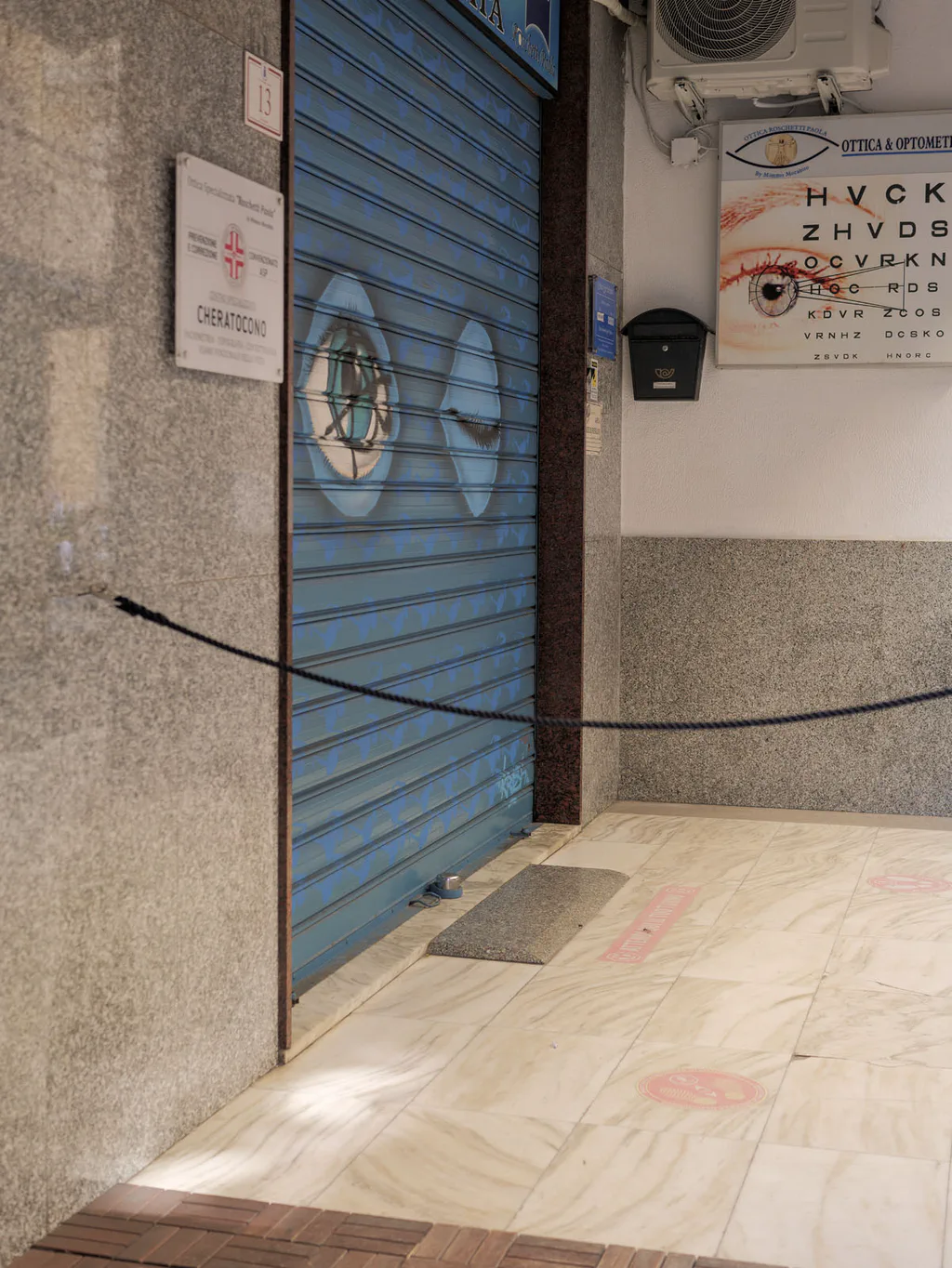 Closed blue shutter of an optician’s shop, the eye chart still on the wall beside it