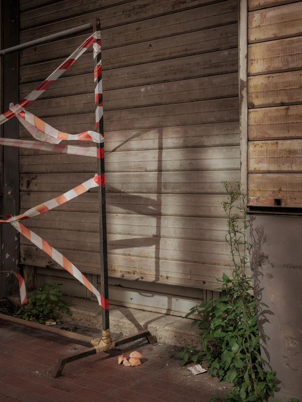 Red and white barrier tape stretched across a metal post in front of a wooden hoarding