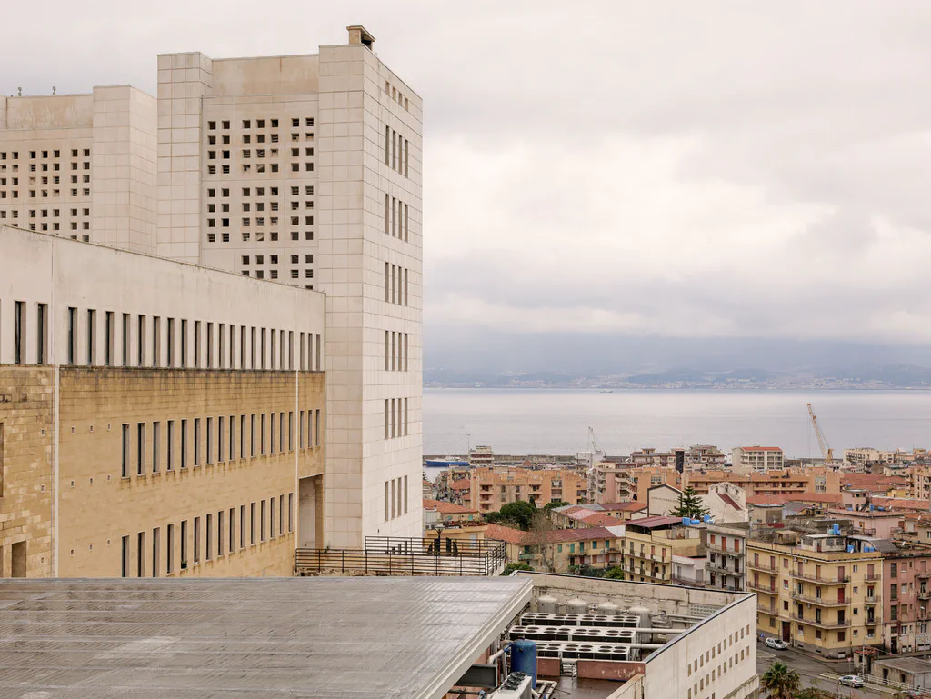 Modernist public building in pale stone, the city and the sea behind it