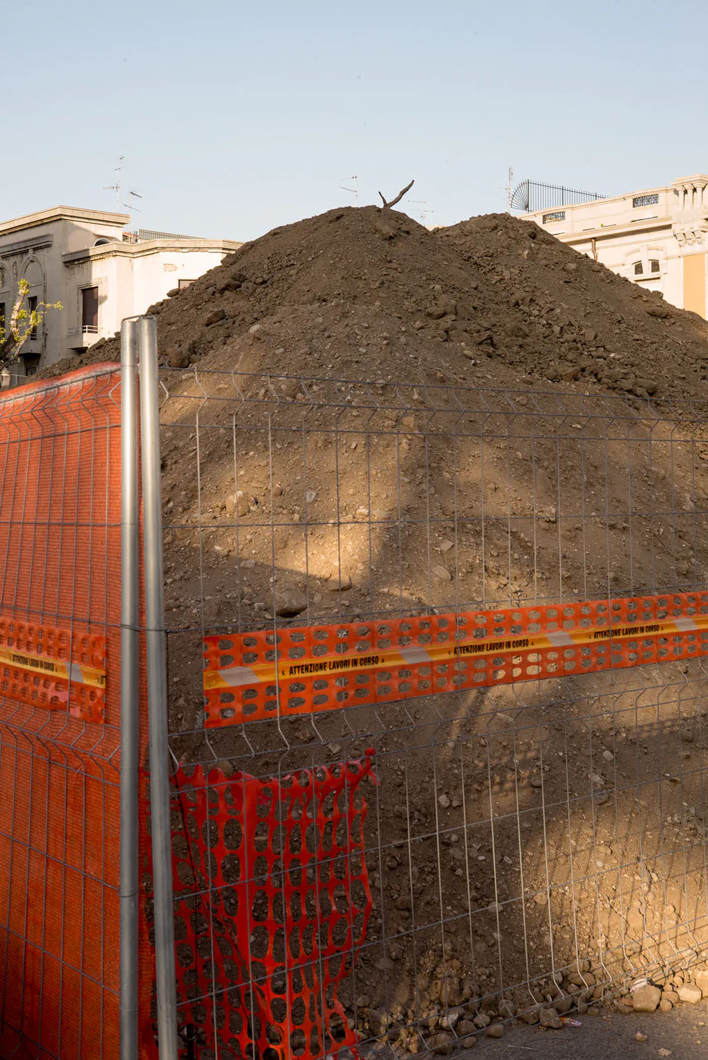 Mound of excavated earth behind an orange site fence