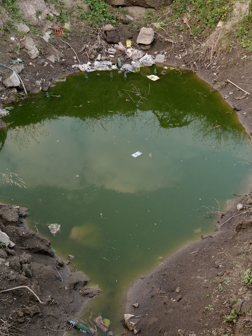 Stagnant green pool in a hollow strewn with rubble and litter