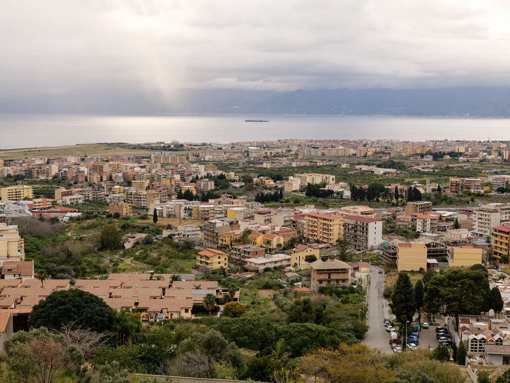 The city spread below towards the sea under a broken sky