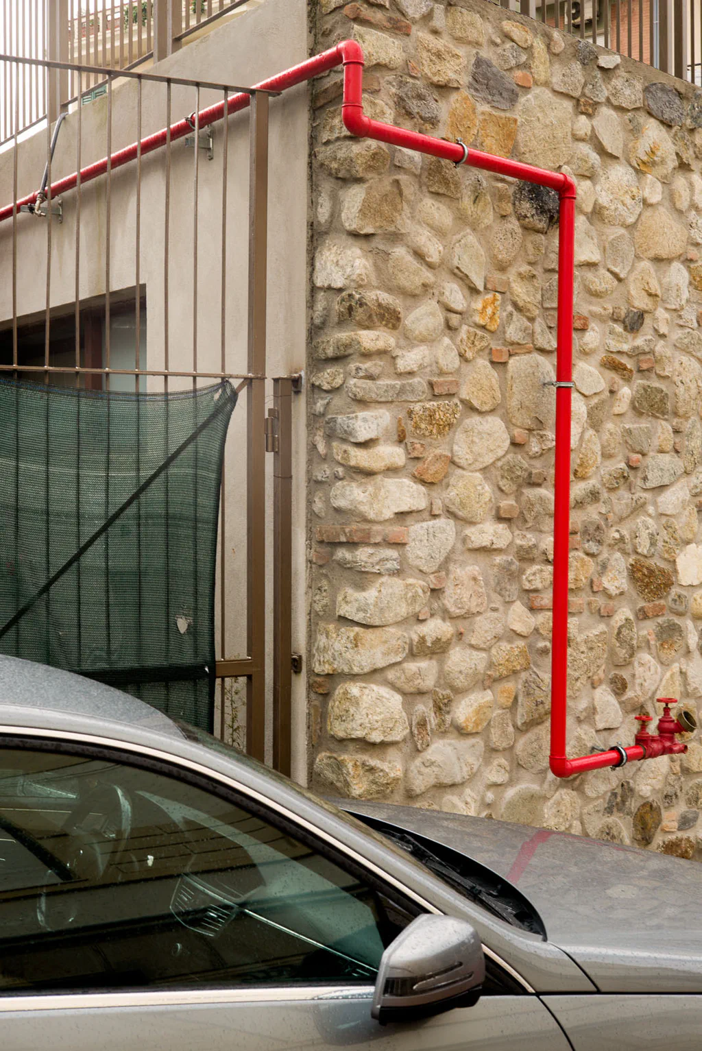 Red pipe running along a stone wall above a parked car