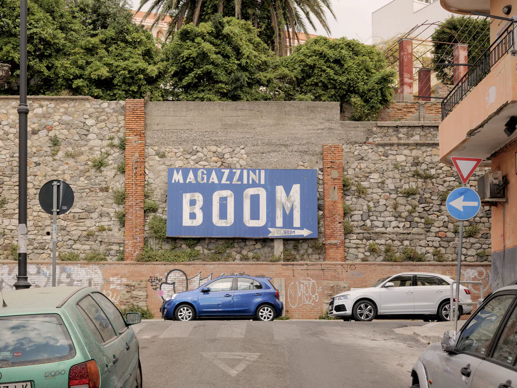 Painted sign reading Magazzini Boom on a stone wall above parked cars