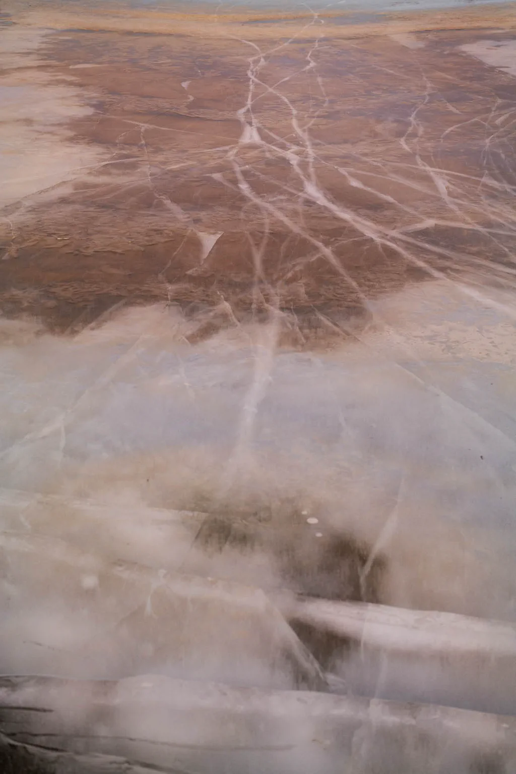 Mineral crust veined with red and white, steam drifting across it