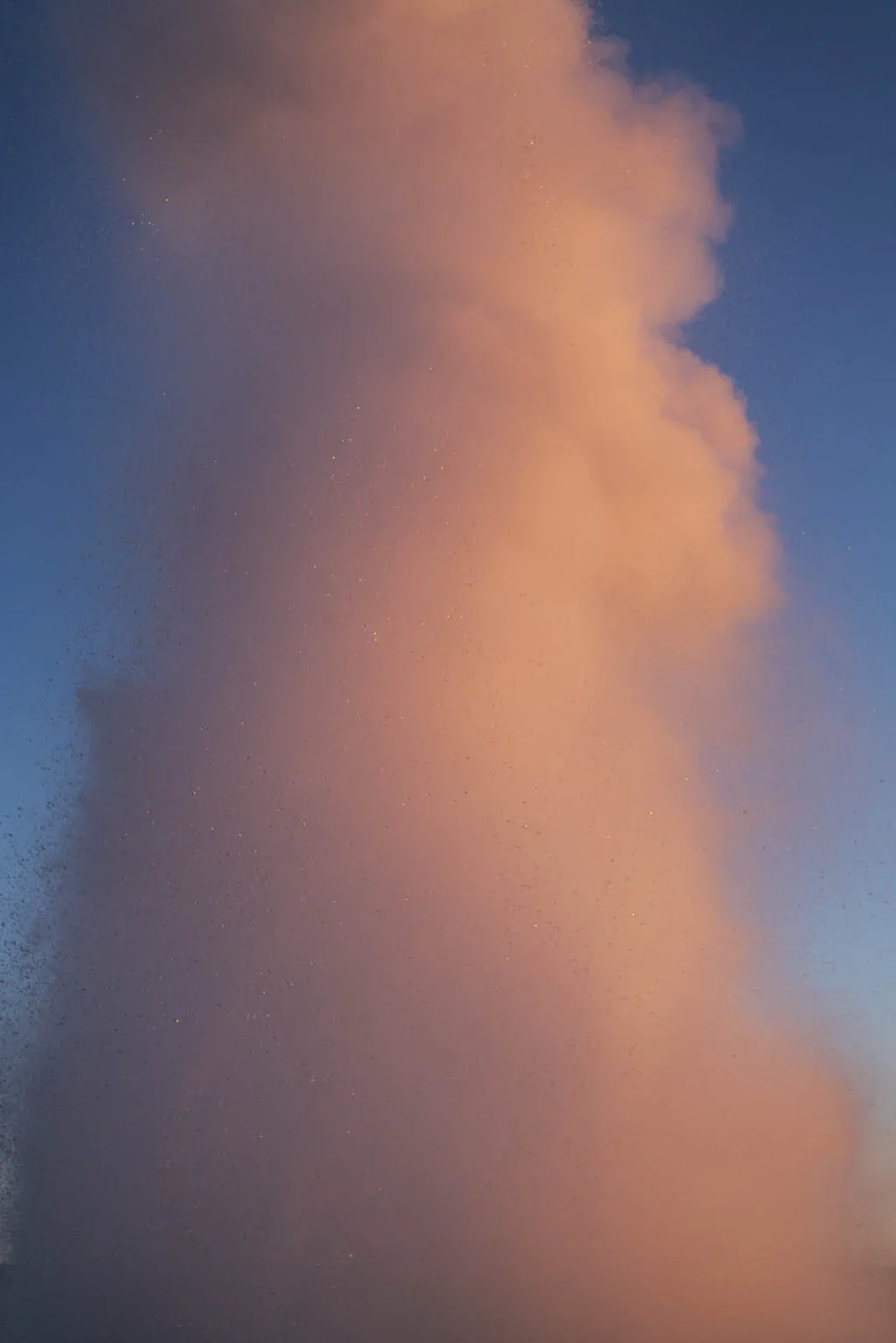 Column of steam turned pink by the low sun against a blue sky