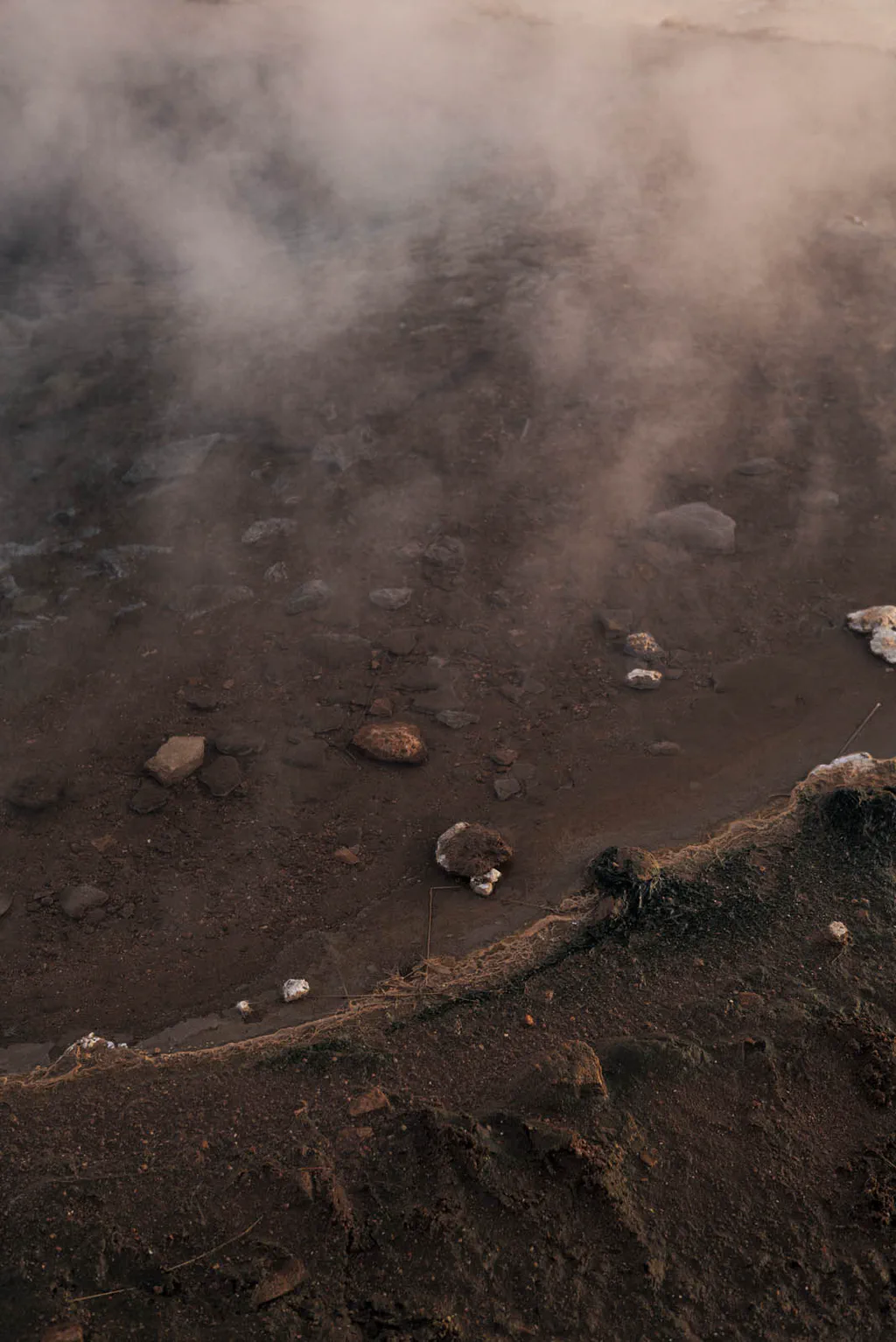 Dark volcanic ground with scattered stones, steam rising beyond