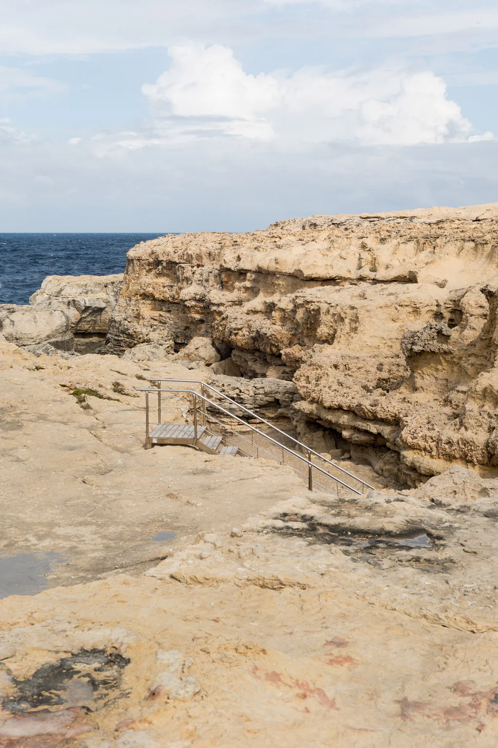 A limestone cliff on the Maltese coast, a metal stair descending towards the sea