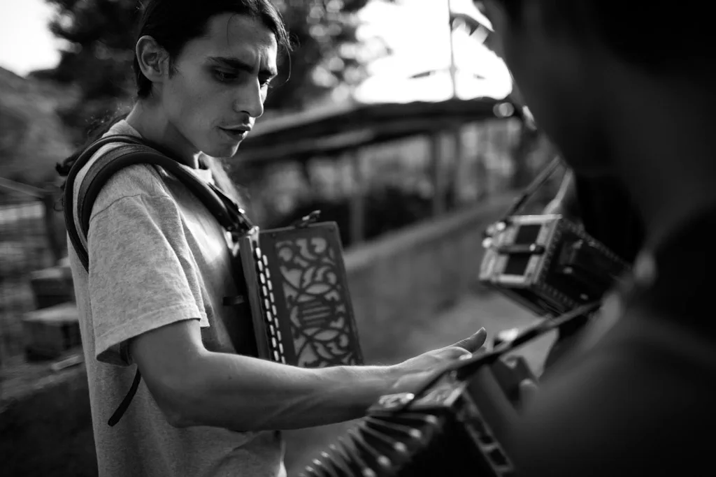 Young man playing a diatonic accordion, another musician beside him